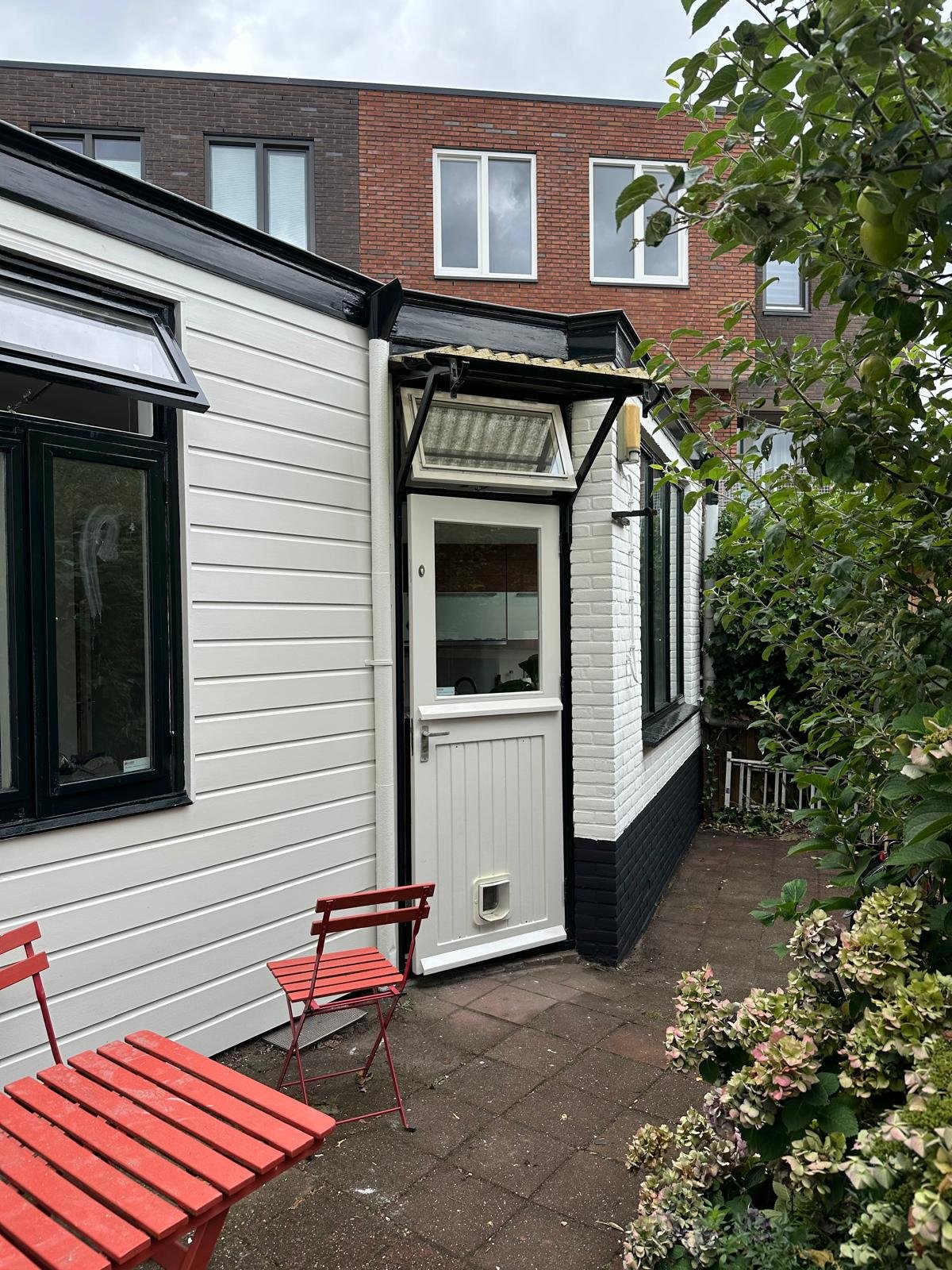 Aanbouw met wit geschilderde gevelbekleding en zwart schilderwerk
